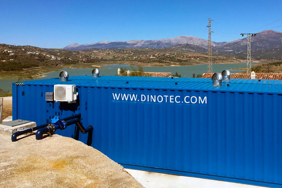 Contenedor industrial azul junto a embalse y montañas