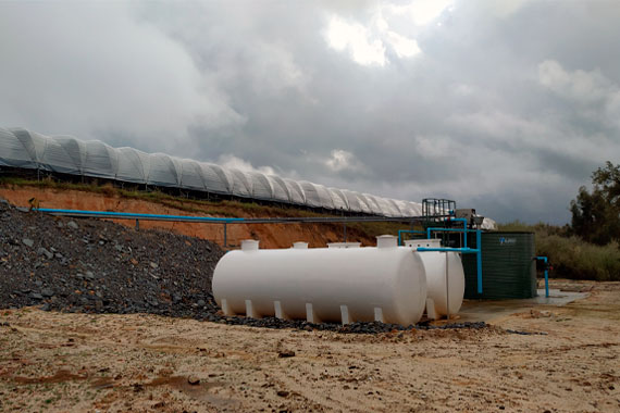Depósitos industriales junto a invernaderos bajo cielo nublado