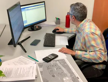 Hombre trabajando en ordenador con documentos y calculadora